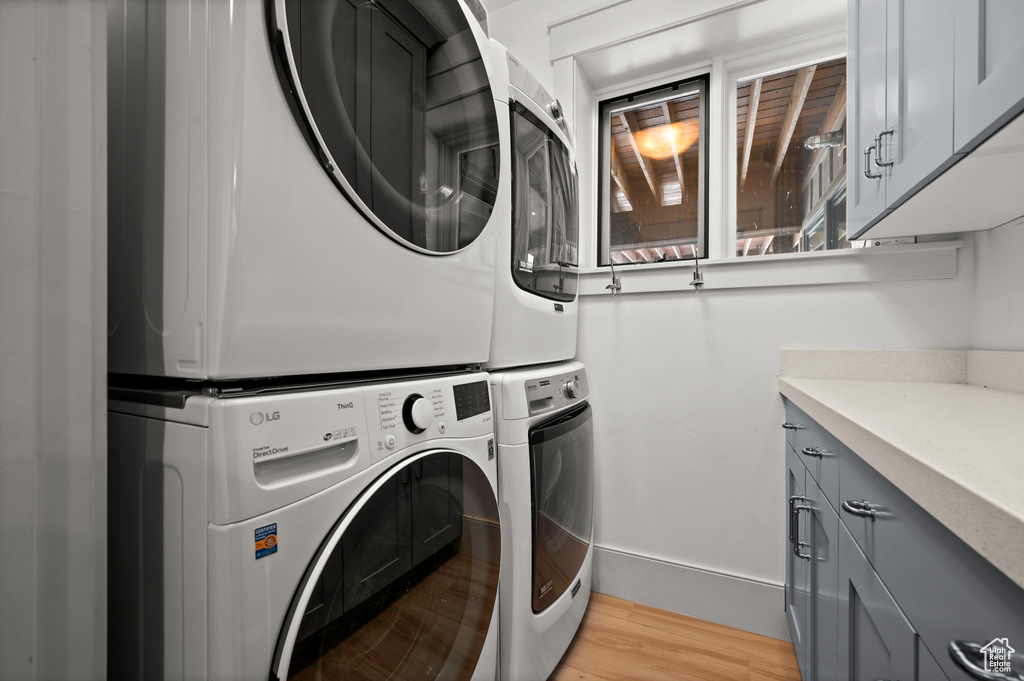 Laundry area featuring stacked washing maching and dryer, cabinets, and light wood-type flooring