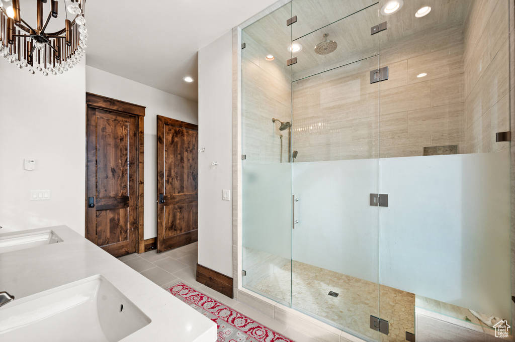 Bathroom featuring a shower with door, a notable chandelier, tile flooring, and double sink