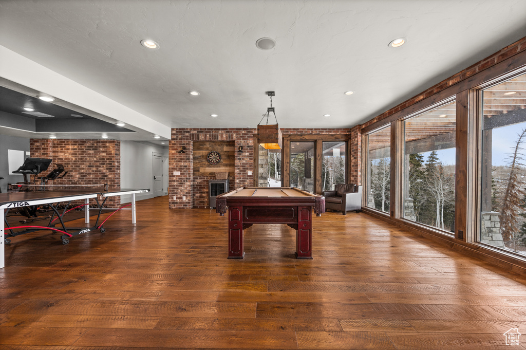Recreation room featuring dark wood-type flooring, brick wall, pool table, and a fireplace