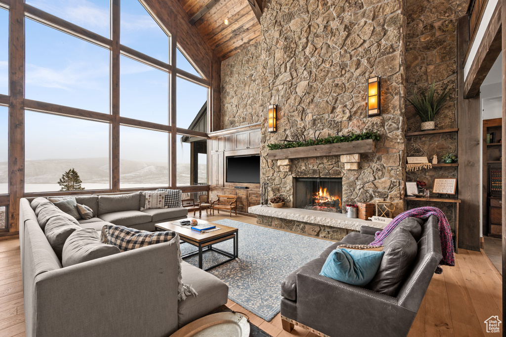 Living room featuring a stone fireplace, light wood-type flooring, high vaulted ceiling, and wooden ceiling