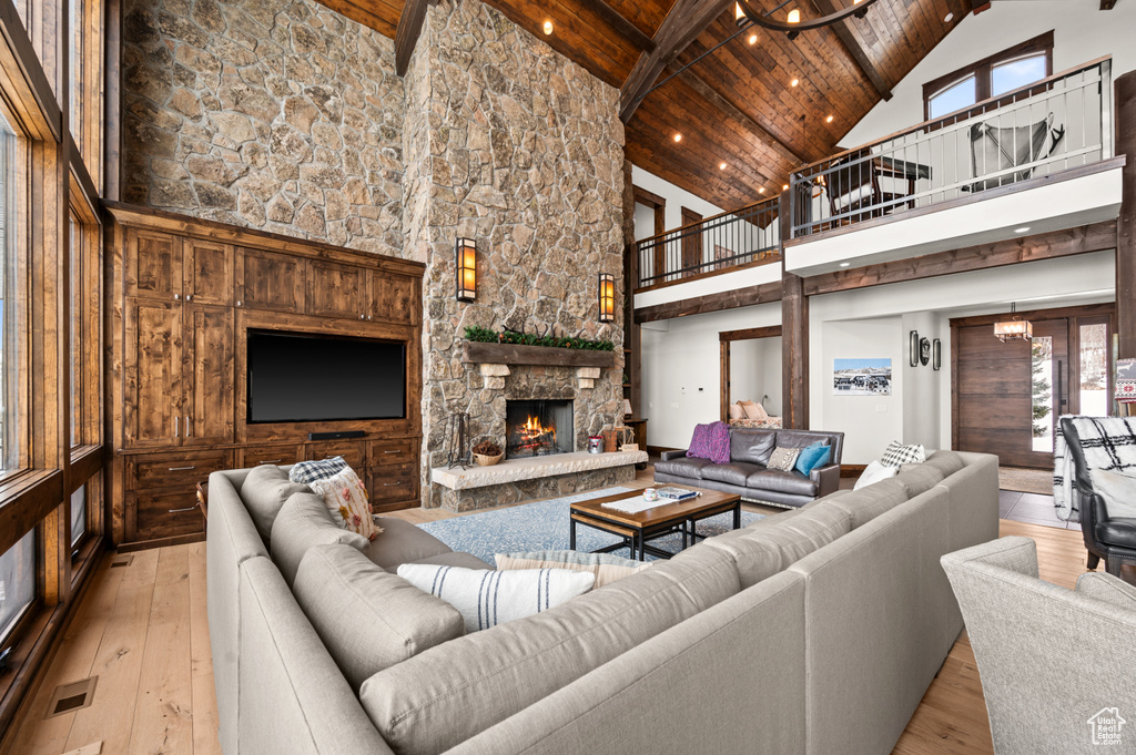 Living room with a stone fireplace, wooden ceiling, light hardwood / wood-style flooring, and high vaulted ceiling