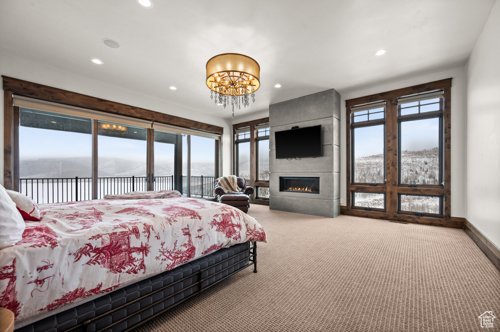 Carpeted bedroom featuring multiple windows, a fireplace, an inviting chandelier, and access to outside