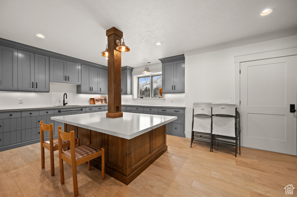 Kitchen featuring hanging light fixtures, light hardwood / wood-style floors, a center island, gray cabinets, and sink
