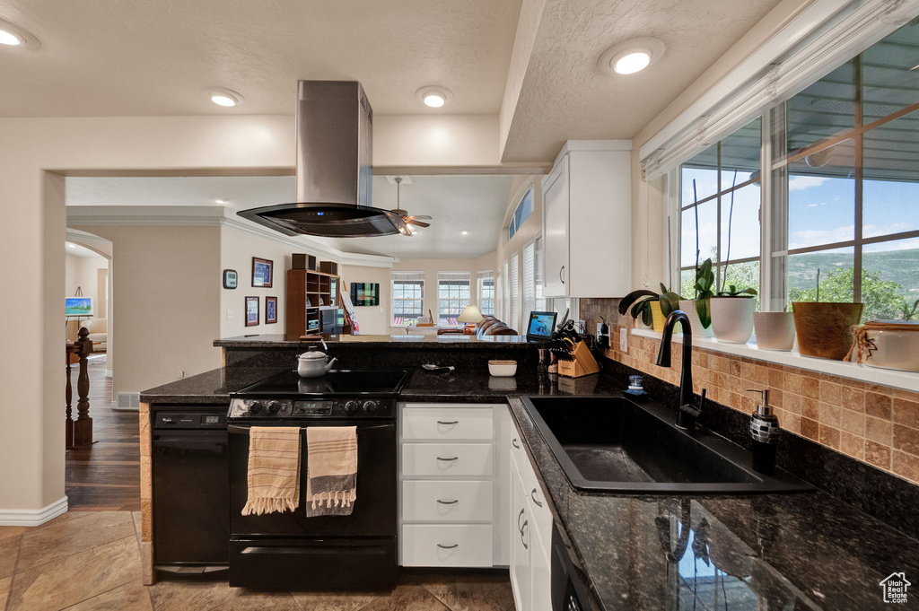 Kitchen with dark stone countertops, white cabinets, black range oven, sink, and island range hood