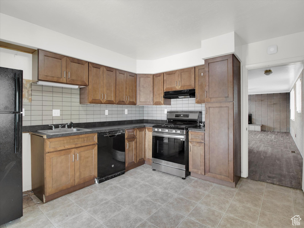 Kitchen featuring tasteful backsplash, range hood, light tile floors, and black appliances