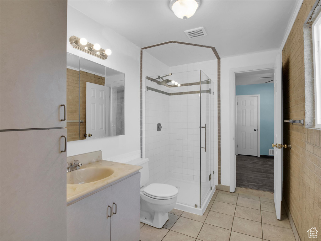 Bathroom featuring toilet, vanity, ceiling fan, a shower with door, and tile floors