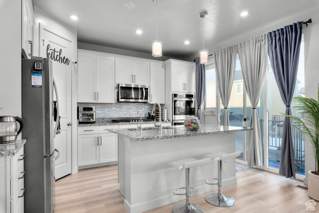 Kitchen with stainless steel appliances, white cabinets, a center island with sink, and light hardwood / wood-style flooring