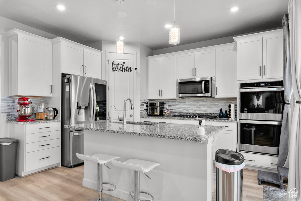 Kitchen featuring light hardwood / wood-style floors, a kitchen island with sink, appliances with stainless steel finishes, white cabinets, and sink