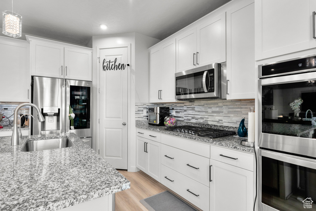 Kitchen featuring tasteful backsplash, hanging light fixtures, light hardwood / wood-style flooring, white cabinets, and stainless steel appliances