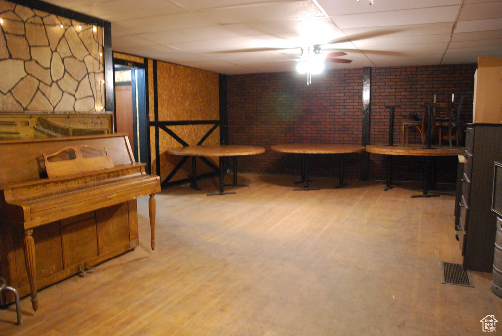 Basement featuring a paneled ceiling, brick wall, light wood-type flooring, and ceiling fan