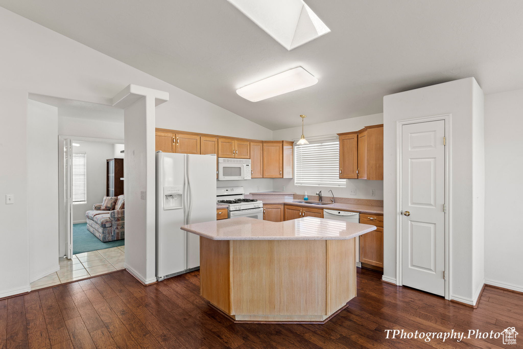 Kitchen featuring vaulted ceiling with skylight, white appliances, a healthy amount of sunlight, sink, and a kitchen island
