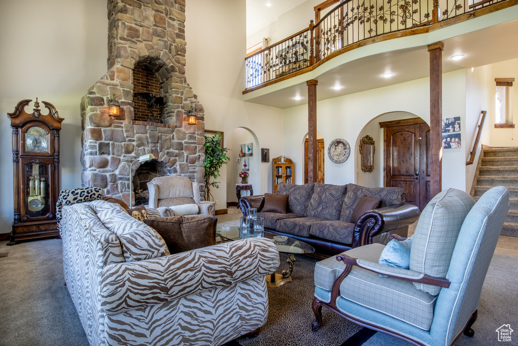 Carpeted living room featuring a stone fireplace, ornate columns, and a high ceiling