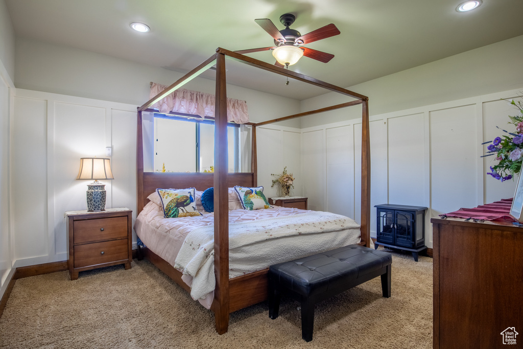 Bedroom featuring a wood stove, light colored carpet, and ceiling fan