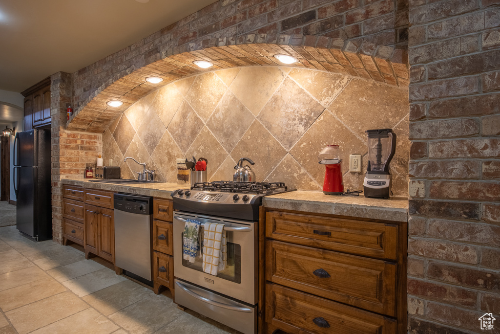 Kitchen featuring sink, brick wall, appliances with stainless steel finishes, and light tile floors