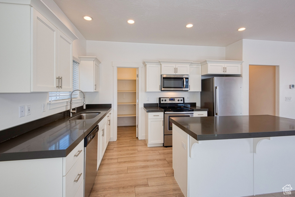 Kitchen featuring white cabinets, appliances with stainless steel finishes, light hardwood / wood-style floors, a center island, and sink