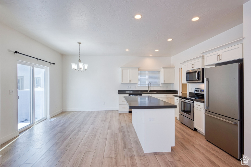 Kitchen with stainless steel appliances, white cabinets, pendant lighting, and a healthy amount of sunlight