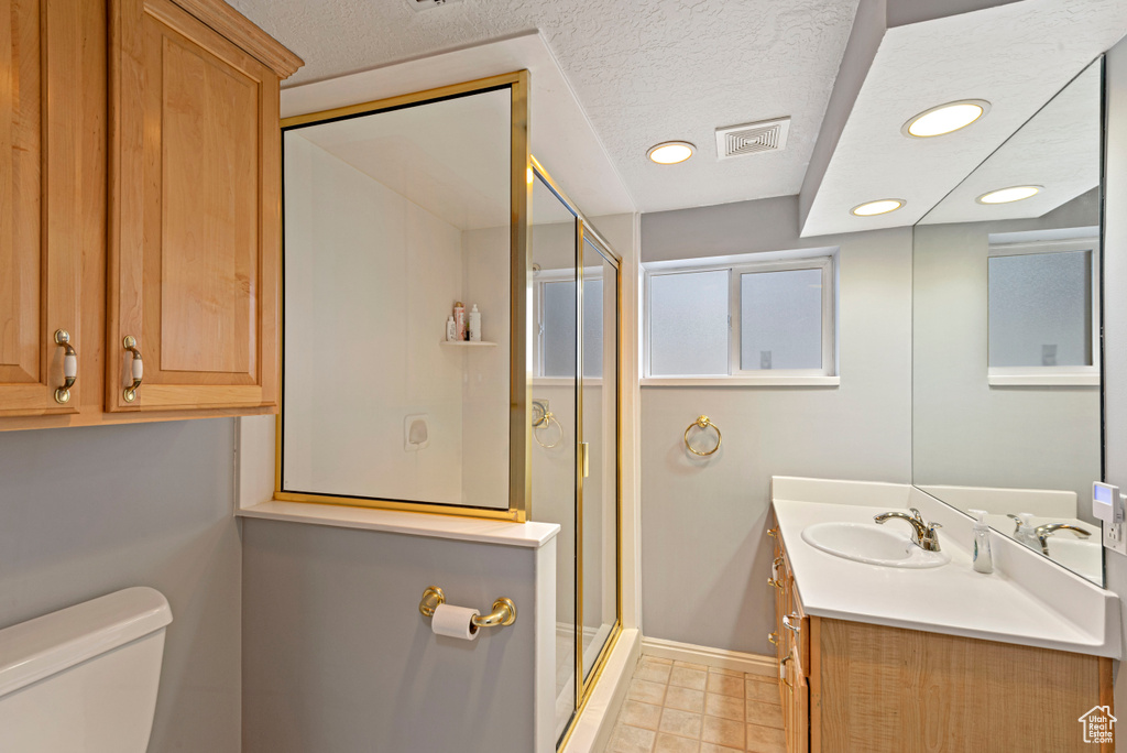 Bathroom with vanity, a textured ceiling, tile floors, toilet, and a shower with shower door