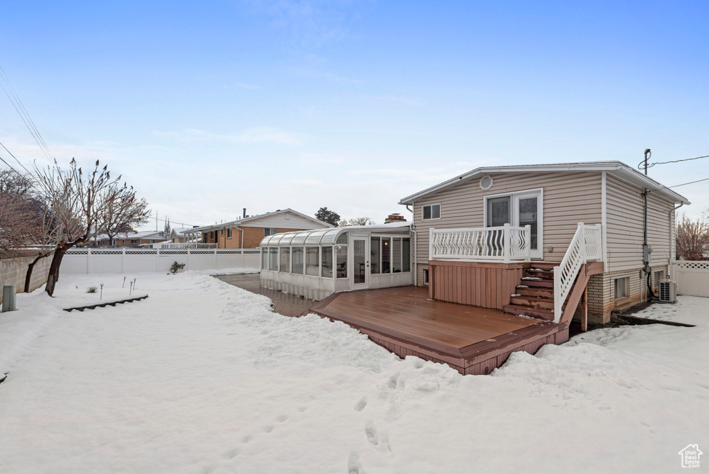 Snow covered property with a wooden deck and a sunroom