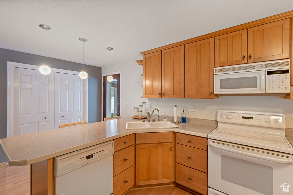 Kitchen with kitchen peninsula, white appliances, pendant lighting, sink, and light wood-type flooring