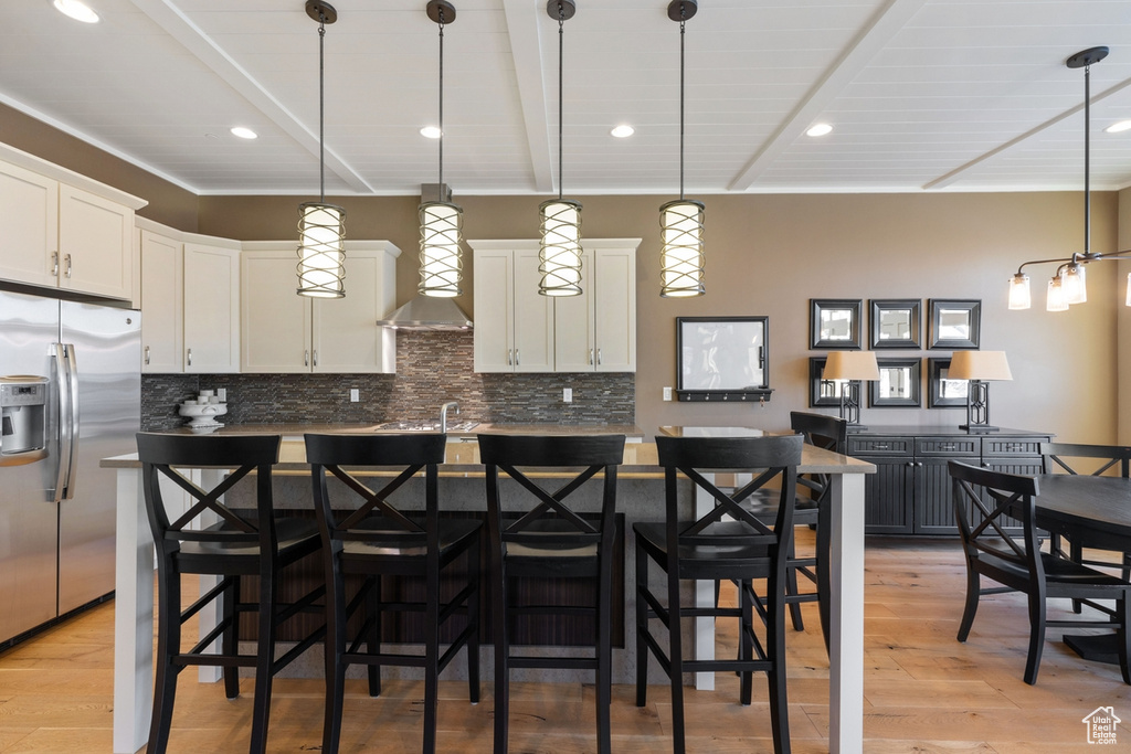 Kitchen featuring wall chimney exhaust hood, tasteful backsplash, stainless steel fridge, and hanging light fixtures