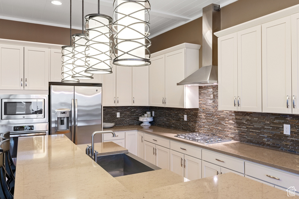 Kitchen featuring wall chimney exhaust hood, appliances with stainless steel finishes, pendant lighting, sink, and tasteful backsplash