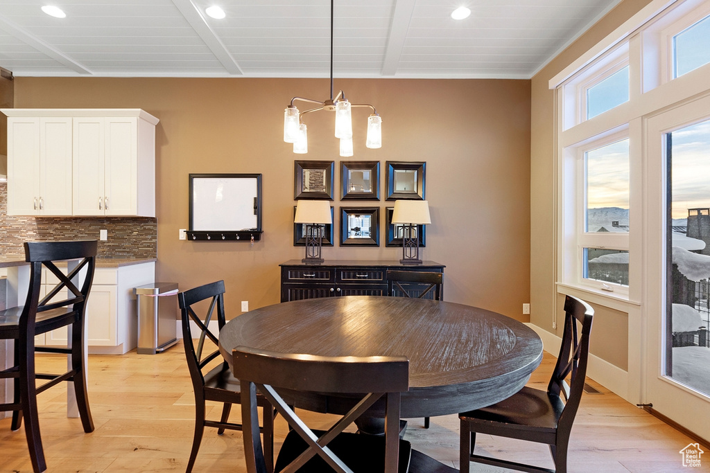 Dining space with a notable chandelier, light hardwood / wood-style floors, and beamed ceiling