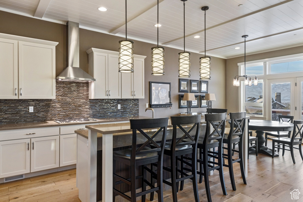 Kitchen with a kitchen breakfast bar, light hardwood / wood-style floors, tasteful backsplash, wall chimney exhaust hood, and decorative light fixtures