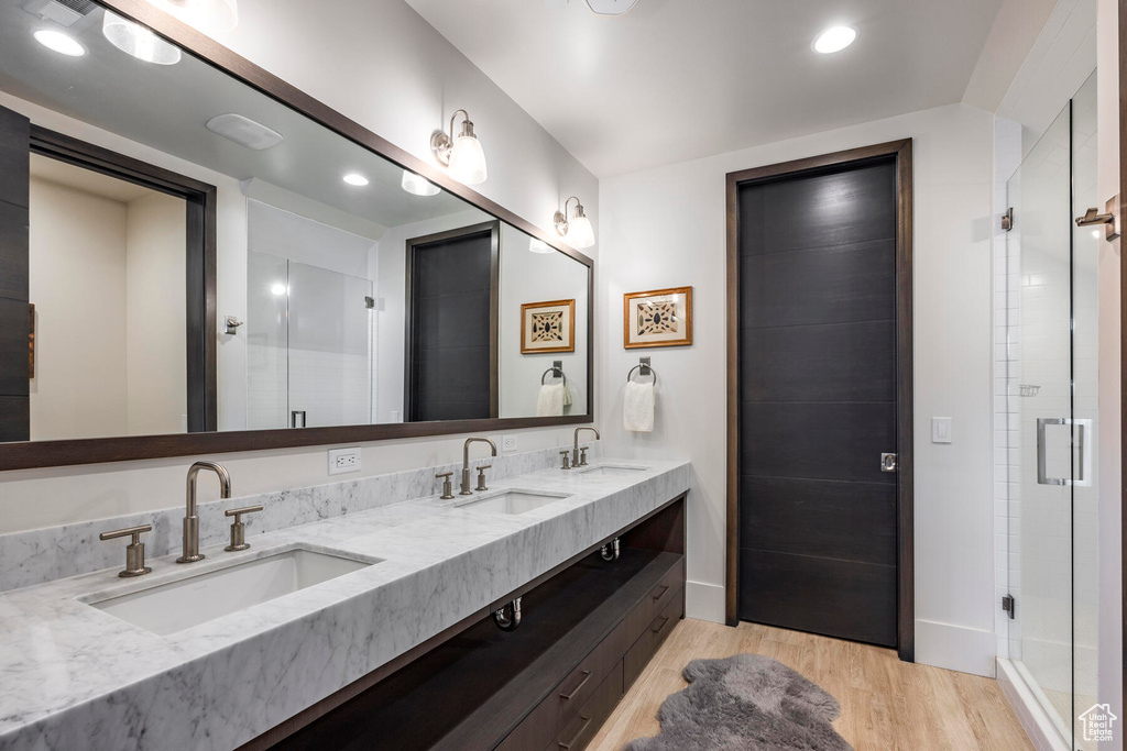 Bathroom with wood-type flooring, a shower with door, and double sink vanity