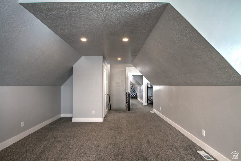 Bonus room with dark carpet, a textured ceiling, and lofted ceiling