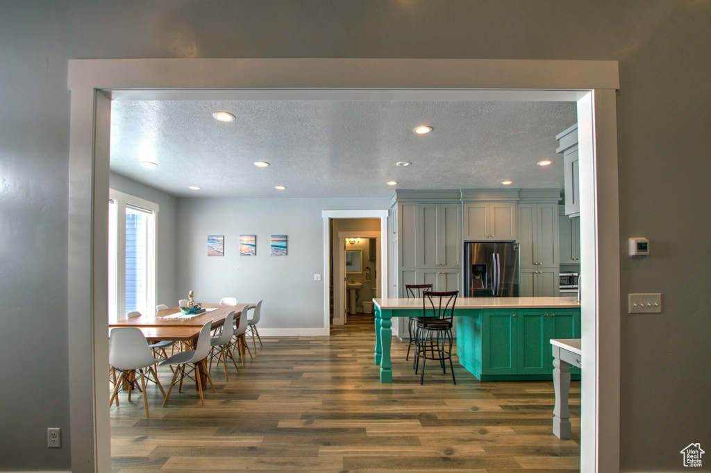 Kitchen featuring stainless steel fridge with ice dispenser, a breakfast bar area, green cabinetry, a textured ceiling, and dark wood-type flooring