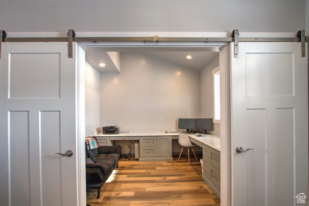 Home office featuring light hardwood / wood-style flooring, a barn door, and vaulted ceiling