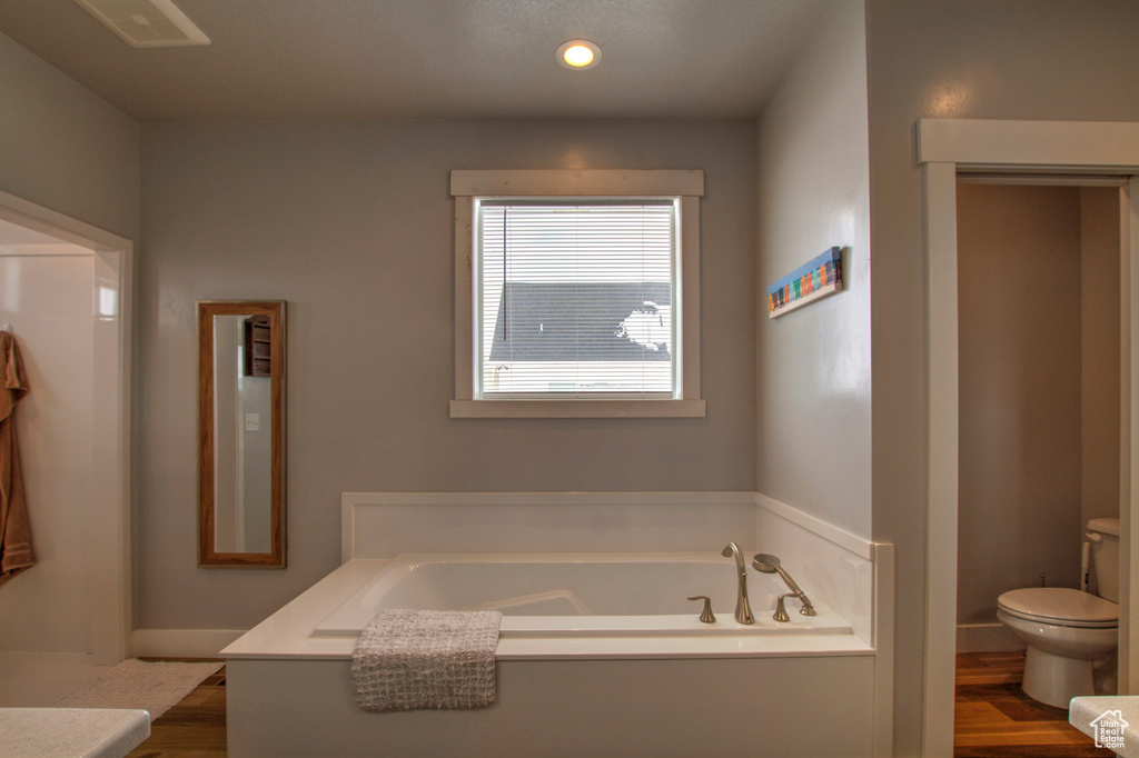 Bathroom featuring toilet, a bath to relax in, and hardwood / wood-style flooring