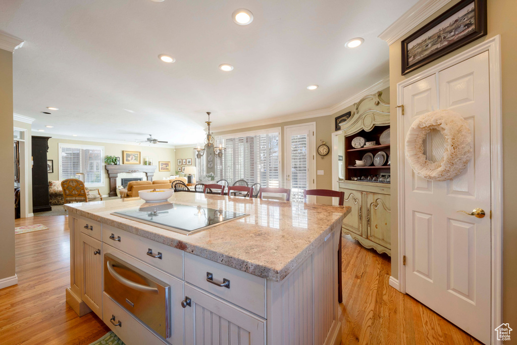 Kitchen featuring crown molding, ceiling fan with notable chandelier, light hardwood / wood-style floors, pendant lighting, and a center island