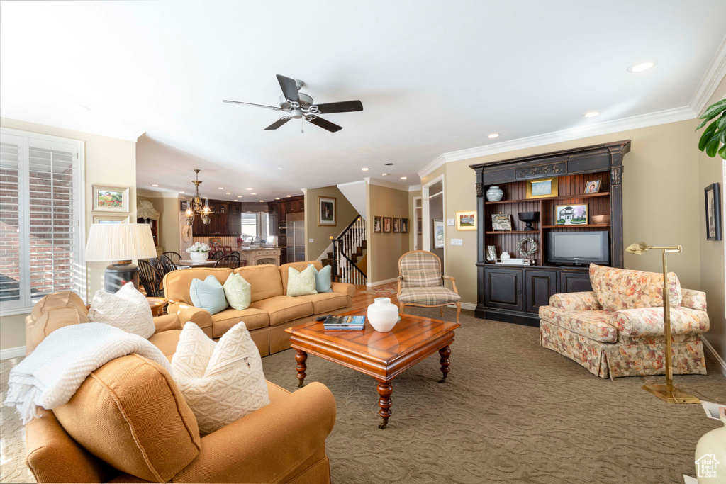 Living room with ornamental molding, carpet floors, and ceiling fan with notable chandelier