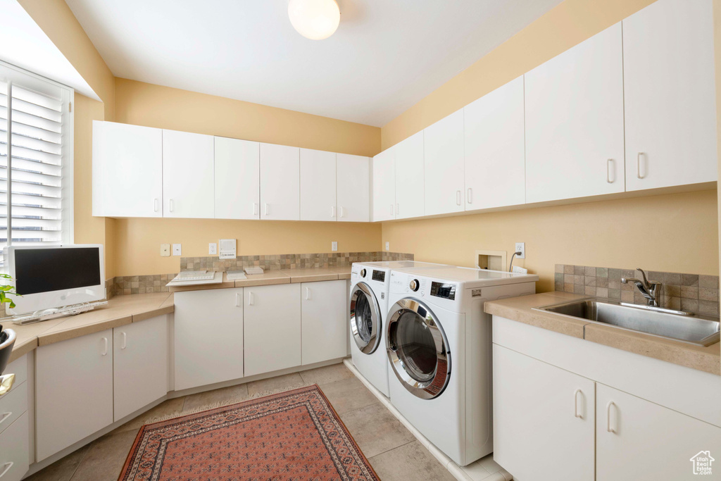 Clothes washing area featuring cabinets, sink, washer and dryer, and light tile floors
