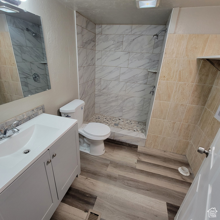 Bathroom featuring wood-type flooring, a tile shower, vanity with extensive cabinet space, and toilet