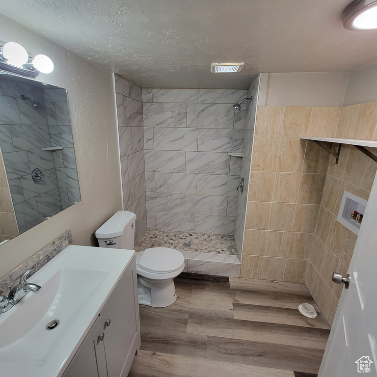 Bathroom with toilet, hardwood / wood-style floors, vanity with extensive cabinet space, tiled shower, and a textured ceiling