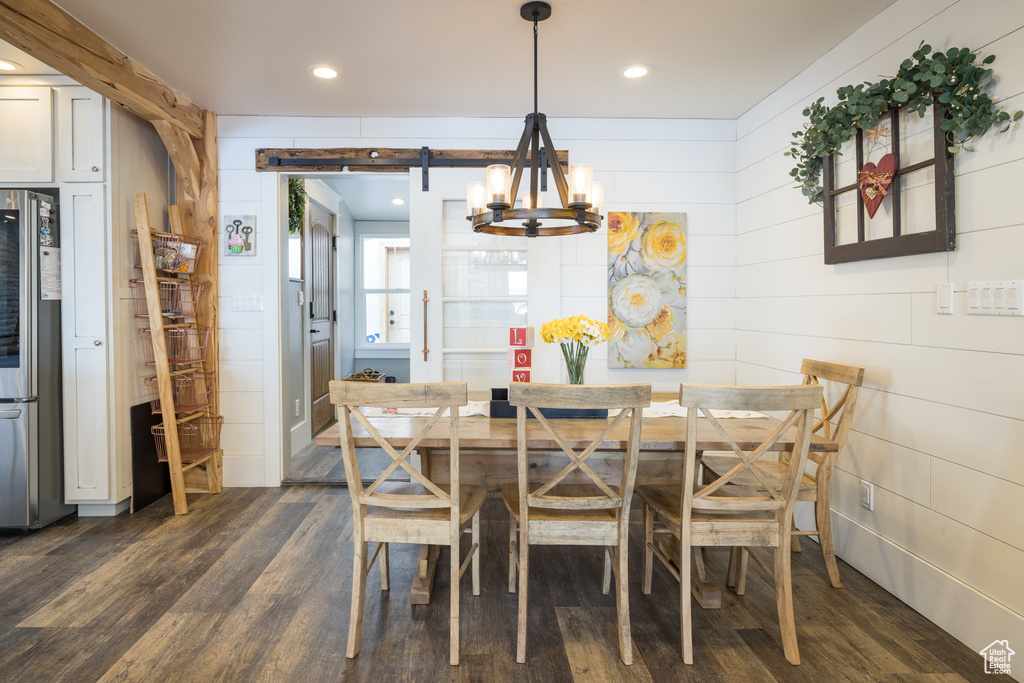 Dining area with wooden walls, a barn door, an inviting chandelier, and dark wood-type flooring
