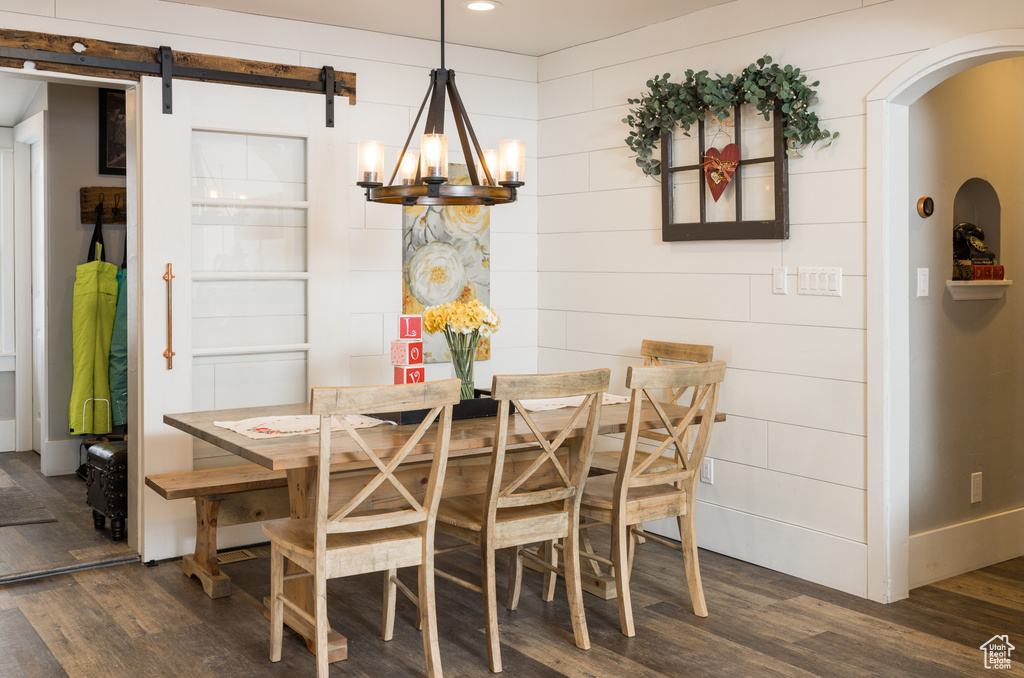 Dining room with dark hardwood / wood-style flooring, a barn door, and a notable chandelier