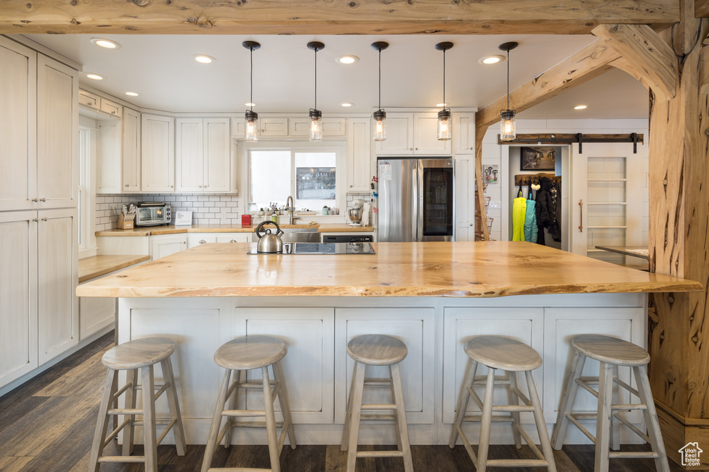 Kitchen featuring stainless steel refrigerator, a barn door, hanging light fixtures, and a kitchen bar