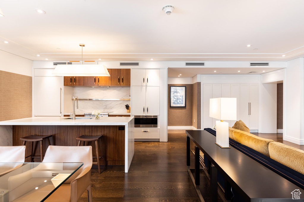 Kitchen featuring hanging light fixtures, white cabinetry, dark hardwood / wood-style flooring, a breakfast bar, and oven