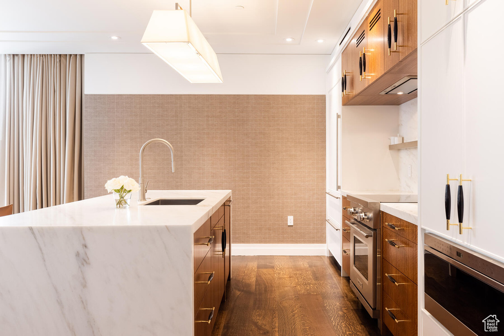 Kitchen with dark hardwood / wood-style flooring, luxury stove, sink, tile walls, and pendant lighting