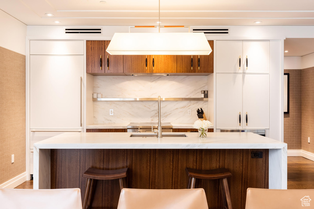 Kitchen with an island with sink, a breakfast bar area, and white cabinetry