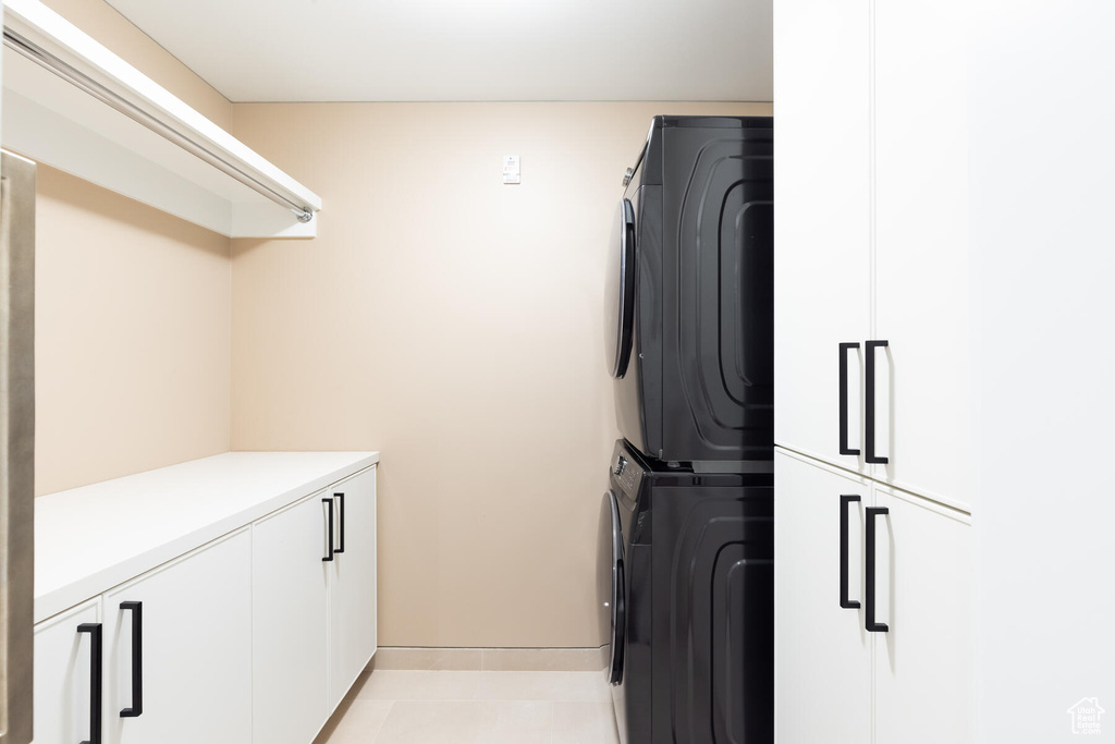Laundry area featuring light tile flooring, stacked washing maching and dryer, and cabinets