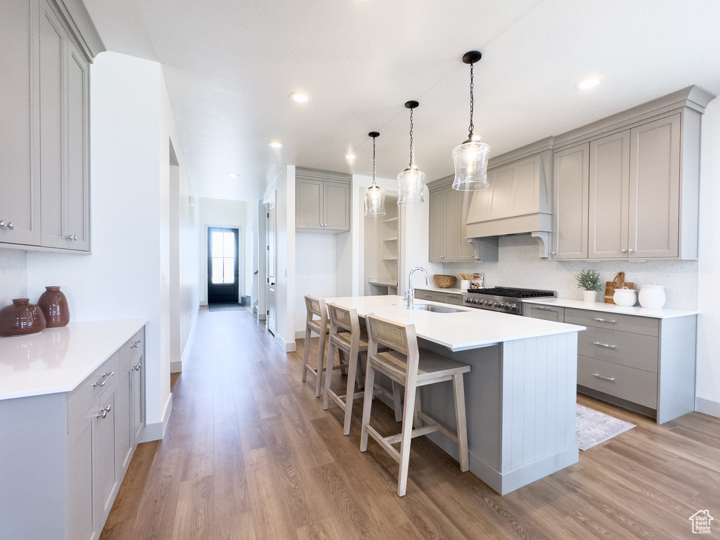 Kitchen featuring hanging light fixtures, light wood-type flooring, range, sink, and custom exhaust hood
