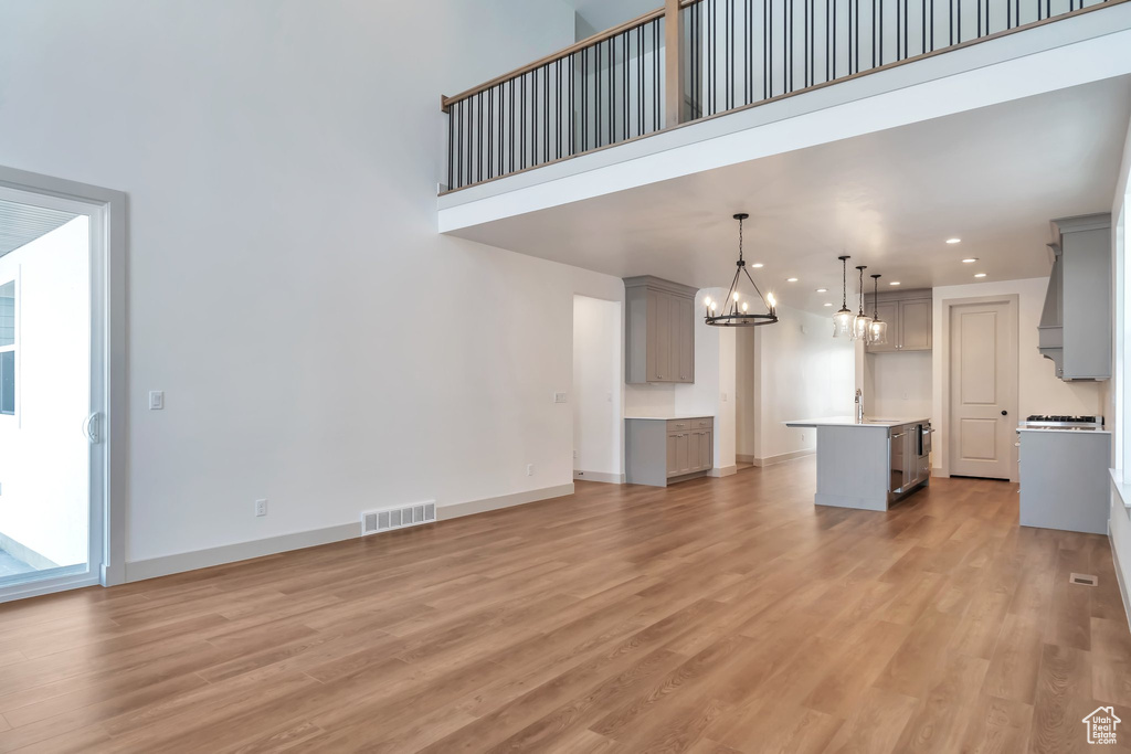 Unfurnished living room featuring a chandelier, sink, light wood-type flooring, and a towering ceiling