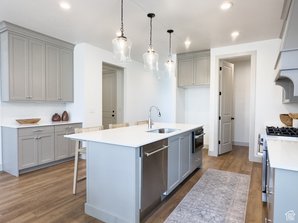 Kitchen featuring decorative light fixtures, a center island with sink, wood-type flooring, sink, and appliances with stainless steel finishes