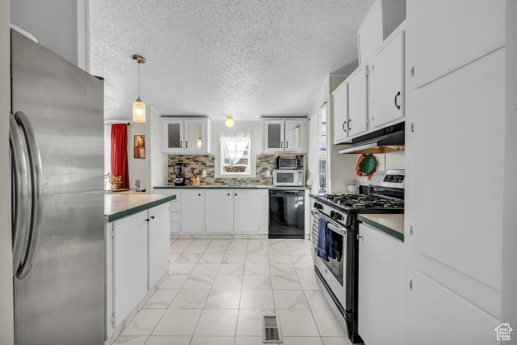 Kitchen with white cabinets, pendant lighting, stainless steel appliances, light tile floors, and tasteful backsplash
