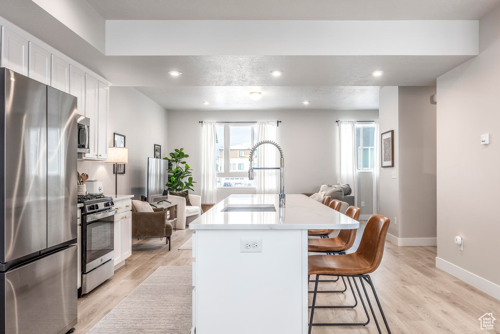 Kitchen featuring appliances with stainless steel finishes, a breakfast bar area, light hardwood / wood-style floors, an island with sink, and white cabinetry