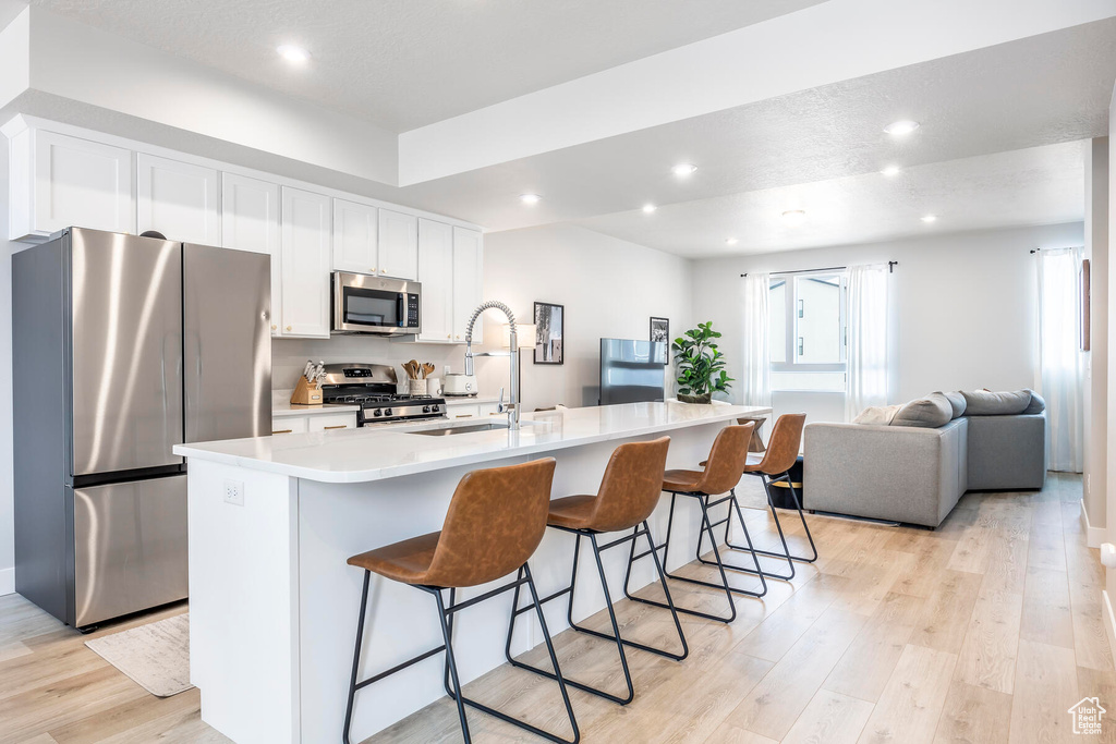 Kitchen with appliances with stainless steel finishes, a kitchen island with sink, white cabinetry, a wealth of natural light, and light wood-type flooring